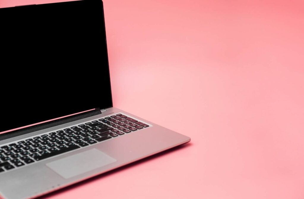 A silver laptop open against a pink background